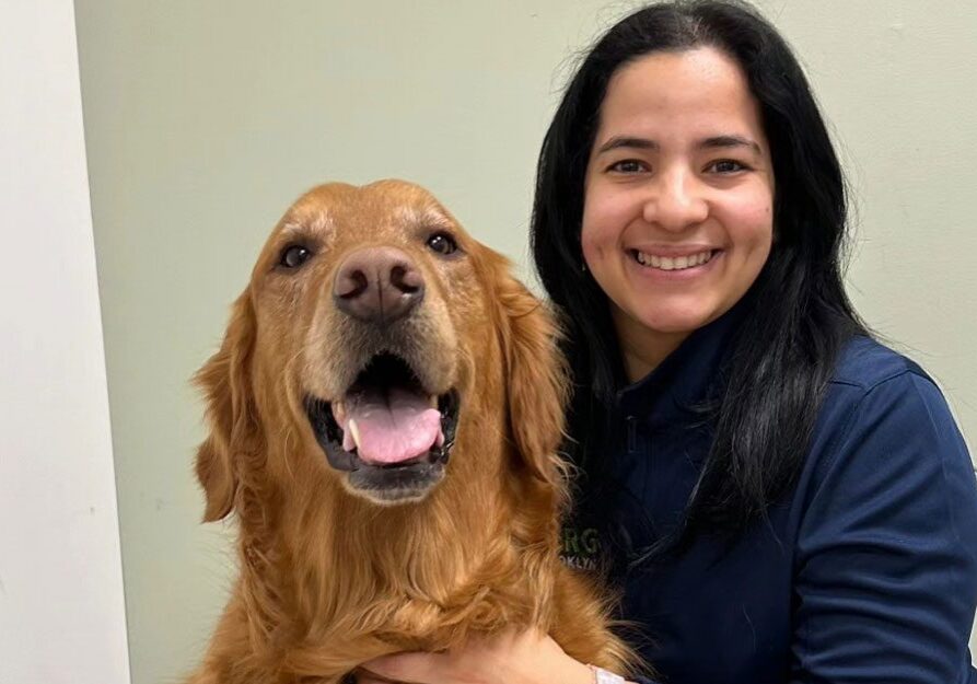 female staff member smiling and posing with golden retriever